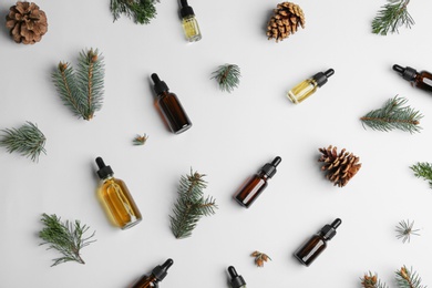 Photo of Different little bottles with essential oils among pine branches on white background, flat lay