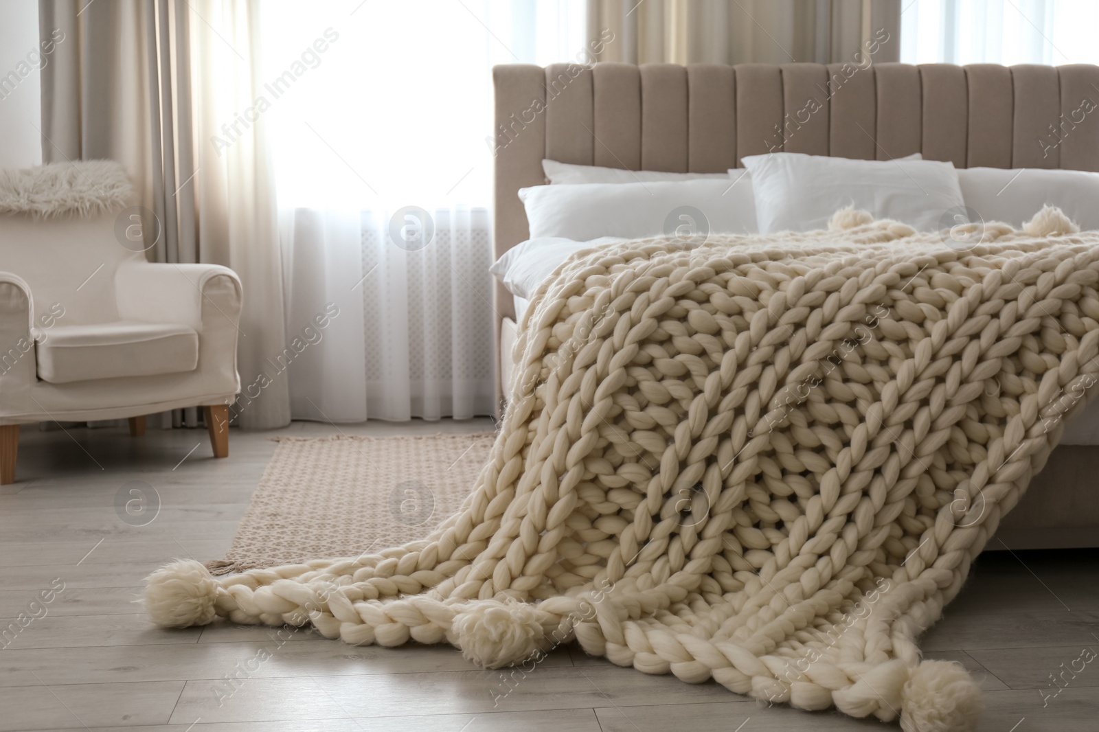 Photo of Soft knitted blanket on bed in room. Interior element