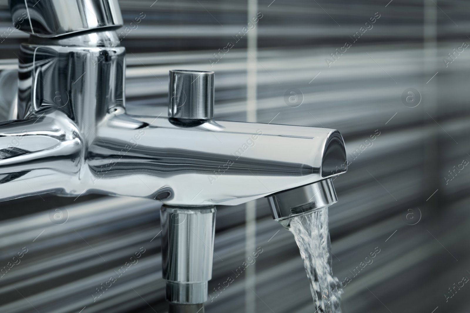 Photo of Water flowing from bath tap on blurred background, closeup