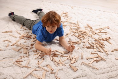 Photo of Cute little boy playing with wooden construction set on carpet at home. Child's toy