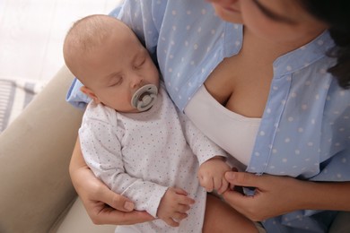 Mother holding her cute sleeping baby with pacifier on armchair, above view