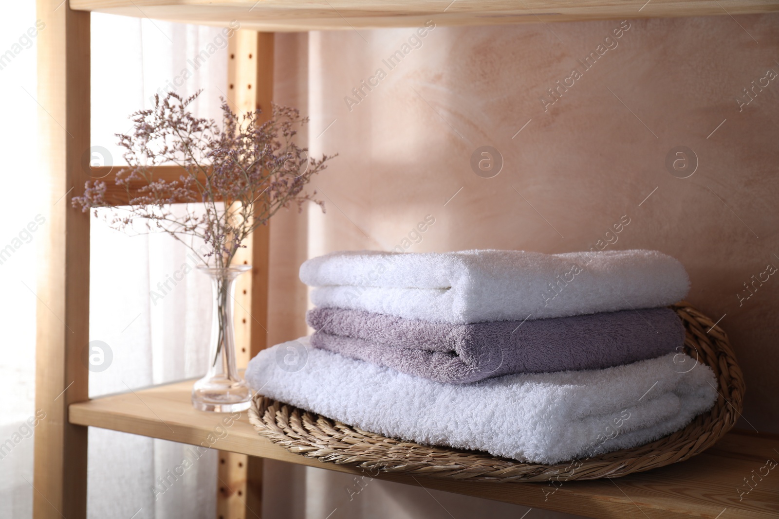 Photo of Stacked soft towels and flowers on wooden shelf indoors