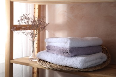 Photo of Stacked soft towels and flowers on wooden shelf indoors