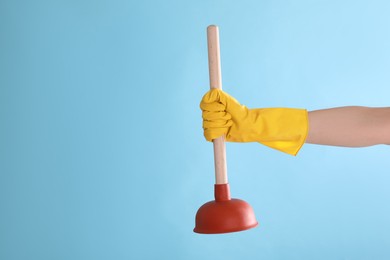 Woman holding plunger on turquoise background, closeup. Space for text