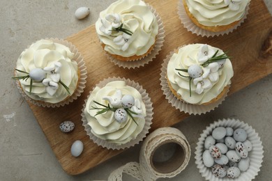 Photo of Tasty Easter cupcakes with vanilla cream, candies and ribbon on gray table, flat lay