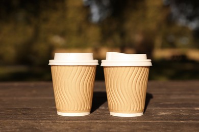 Photo of Paper cups on wooden table in park. Coffee to go