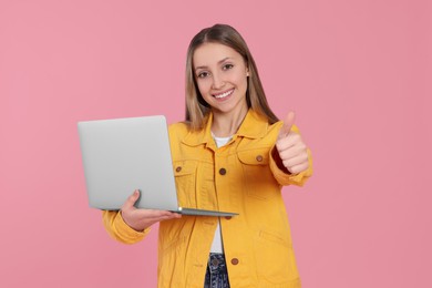Beautiful teenage girl with laptop showing thumb up on pink background