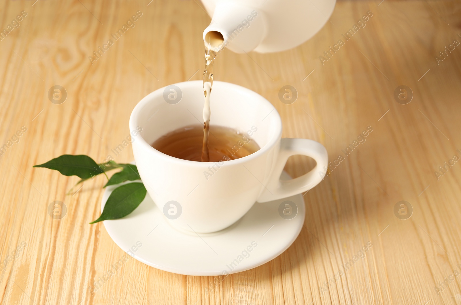 Photo of Pouring tasty tea into cup at light wooden table, closeup