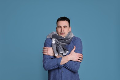 Photo of Young man with scarf suffering from fever on blue background. Cold symptoms