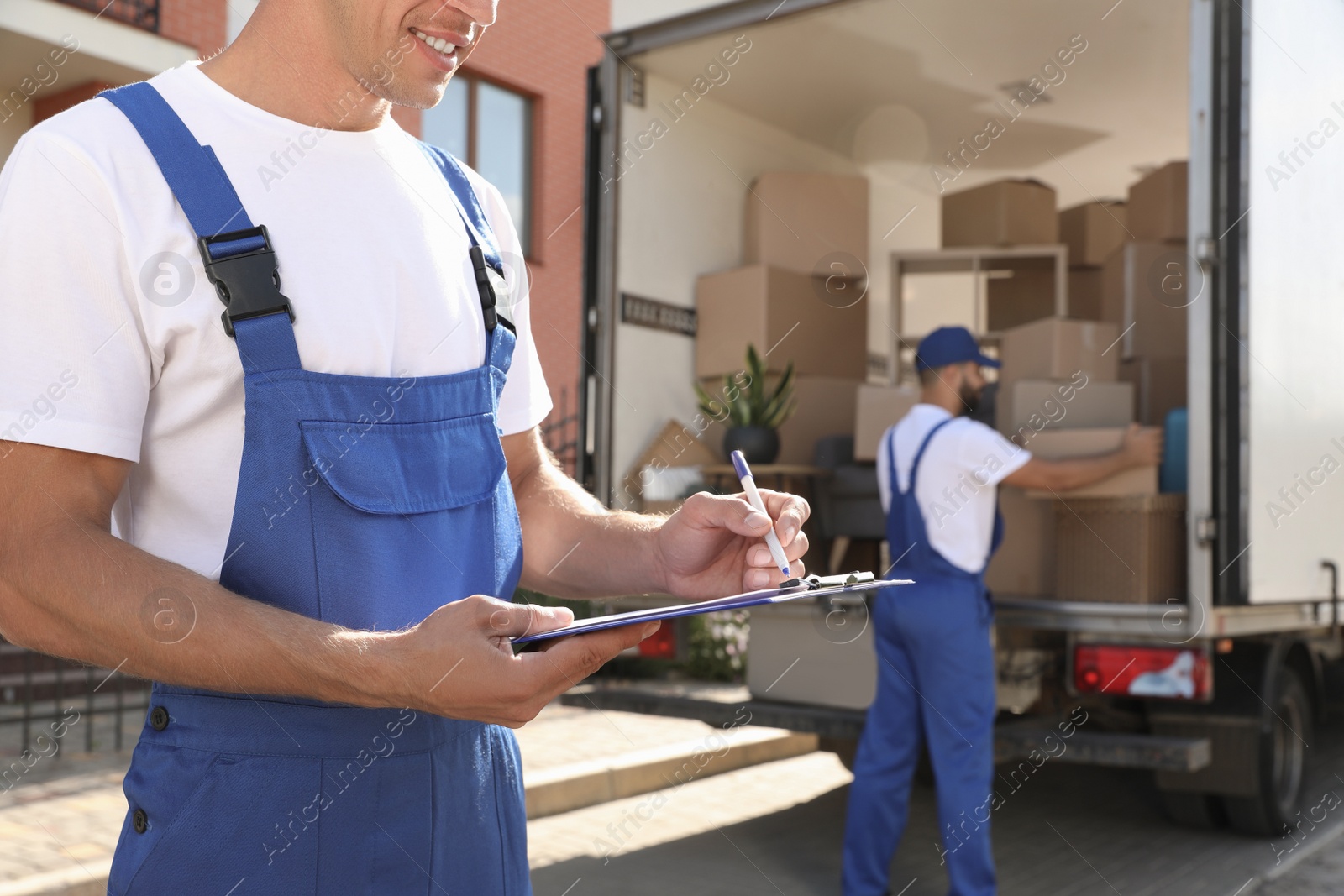 Photo of Moving service workers outdoors, unloading boxes and checking list