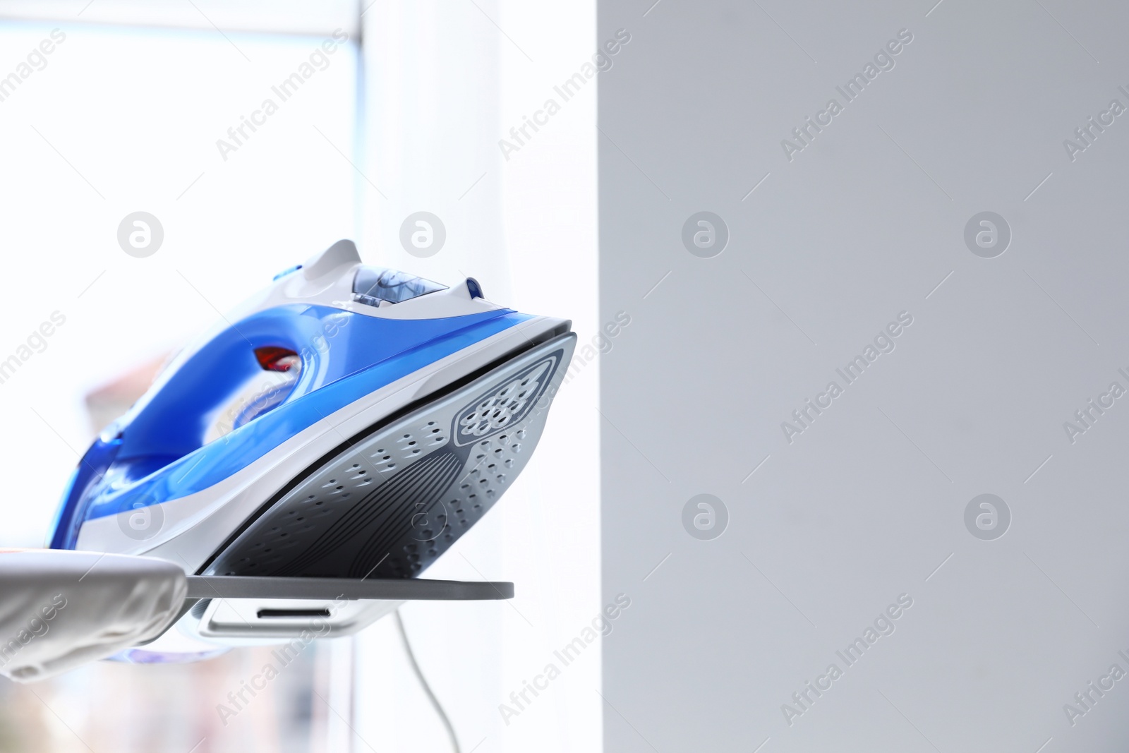 Photo of Modern electric iron on board indoors, space for text. Household appliance