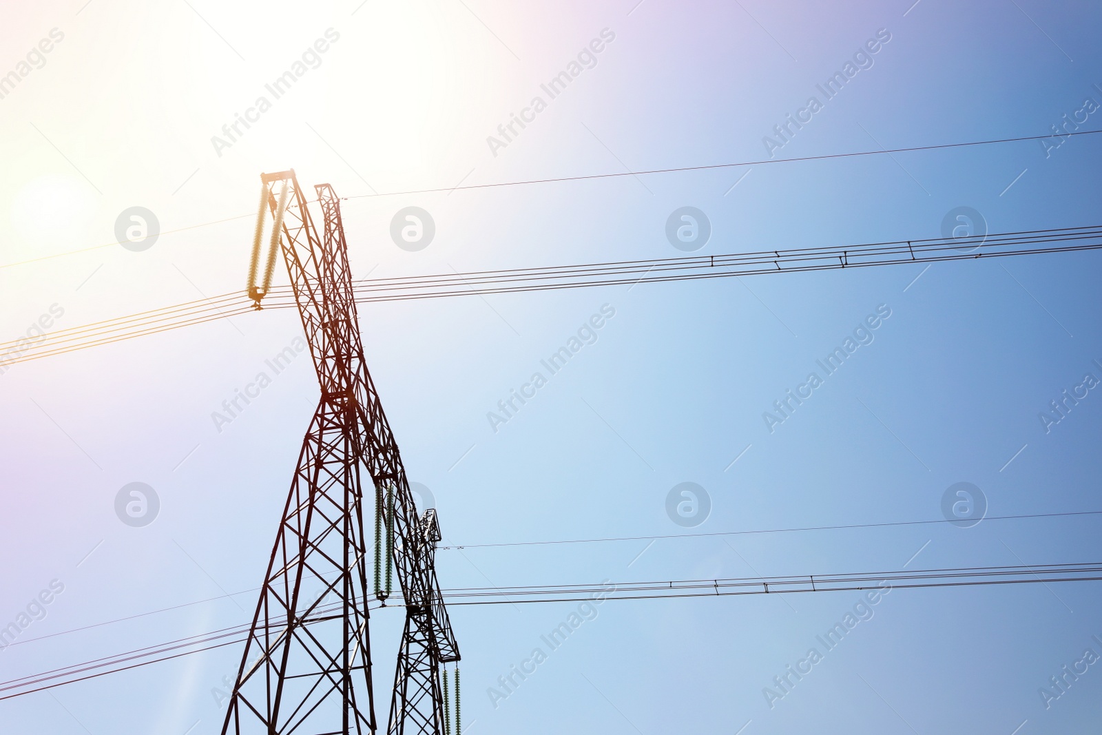 Photo of High voltage tower with electricity transmission power lines against blue sky, low angle view