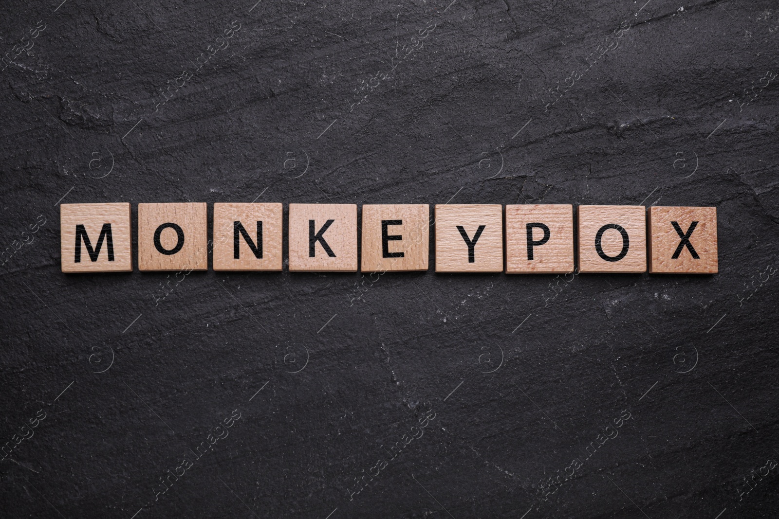 Photo of Word Monkeypox made of wooden squares on black background, top view