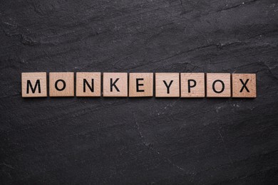 Photo of Word Monkeypox made of wooden squares on black background, top view