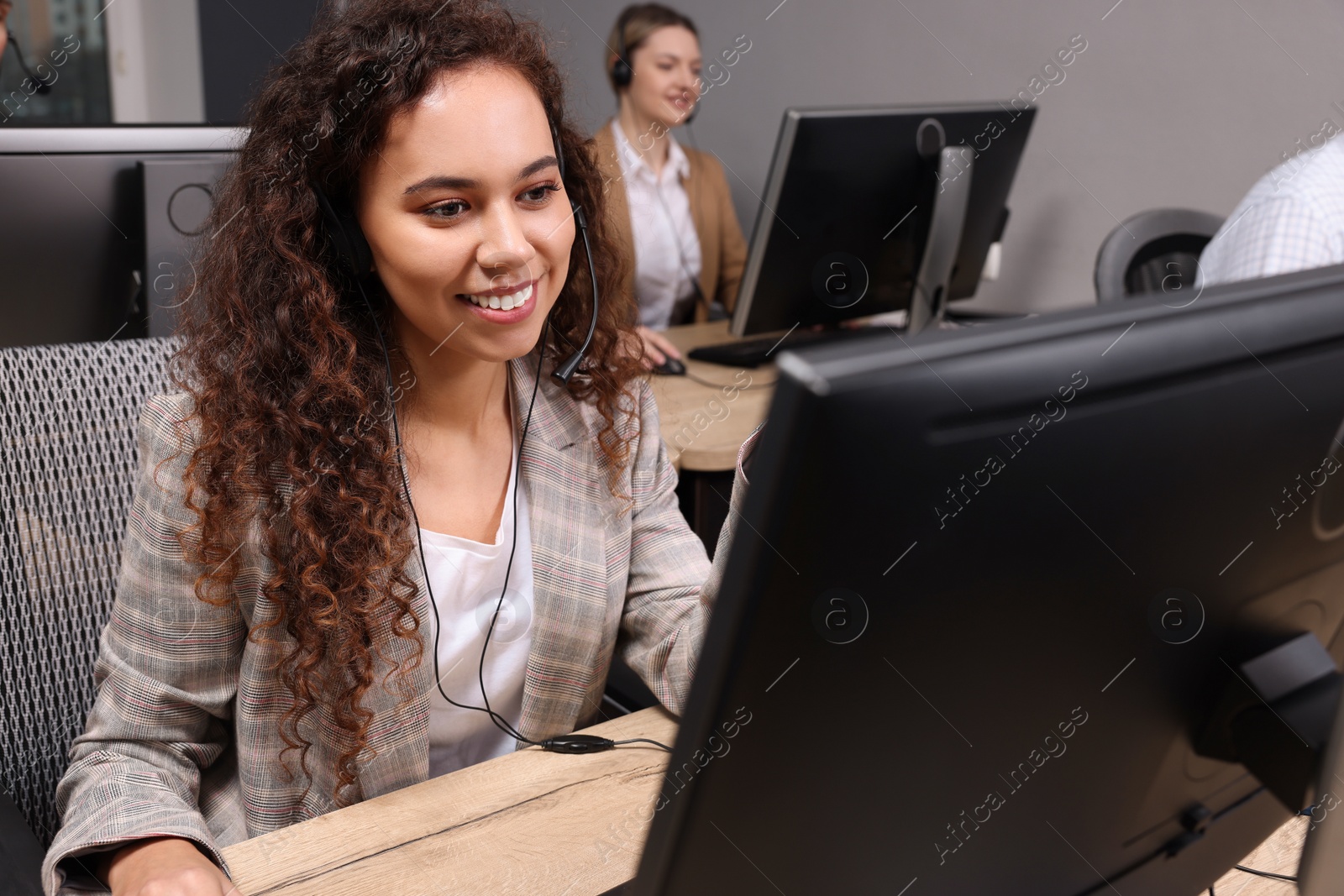 Photo of African American call center operator with headset and her colleagues working in modern office