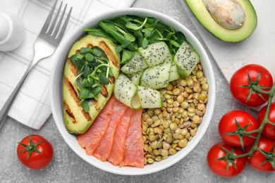 Photo of Delicious lentil bowl with salmon, avocado and cucumber on grey table, flat lay