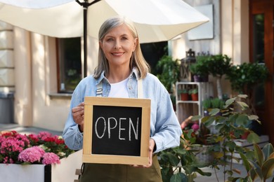 Photo of Happy business owner holding open sign near her flower shop outdoors, space for text