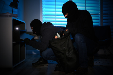 Photo of Thieves taking money and laptop out of steel safe indoors at night