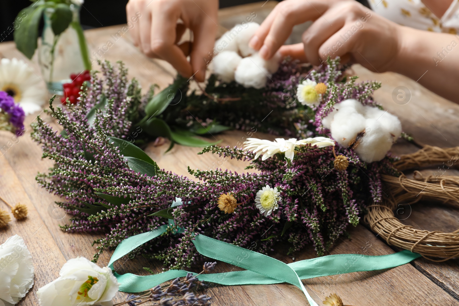 Photo of Florist making beautiful autumnal wreath with heather flowers at wooden table, closeup