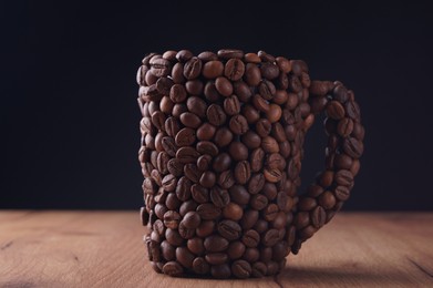 Photo of Cup made of coffee beans on wooden table against black background