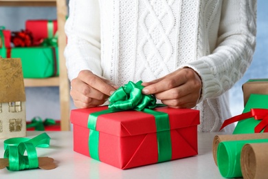 Photo of Woman wrapping Christmas gift at white wooden table indoors, closeup