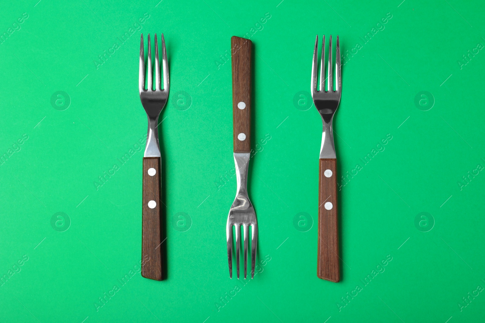 Photo of Forks with wooden handles on green background, flat lay