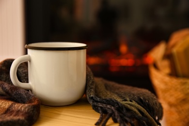 Photo of Mug with hot drink and plaid against fireplace, space for text