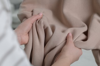 Photo of Woman touching clothes made of soft beige fabric indoors, closeup