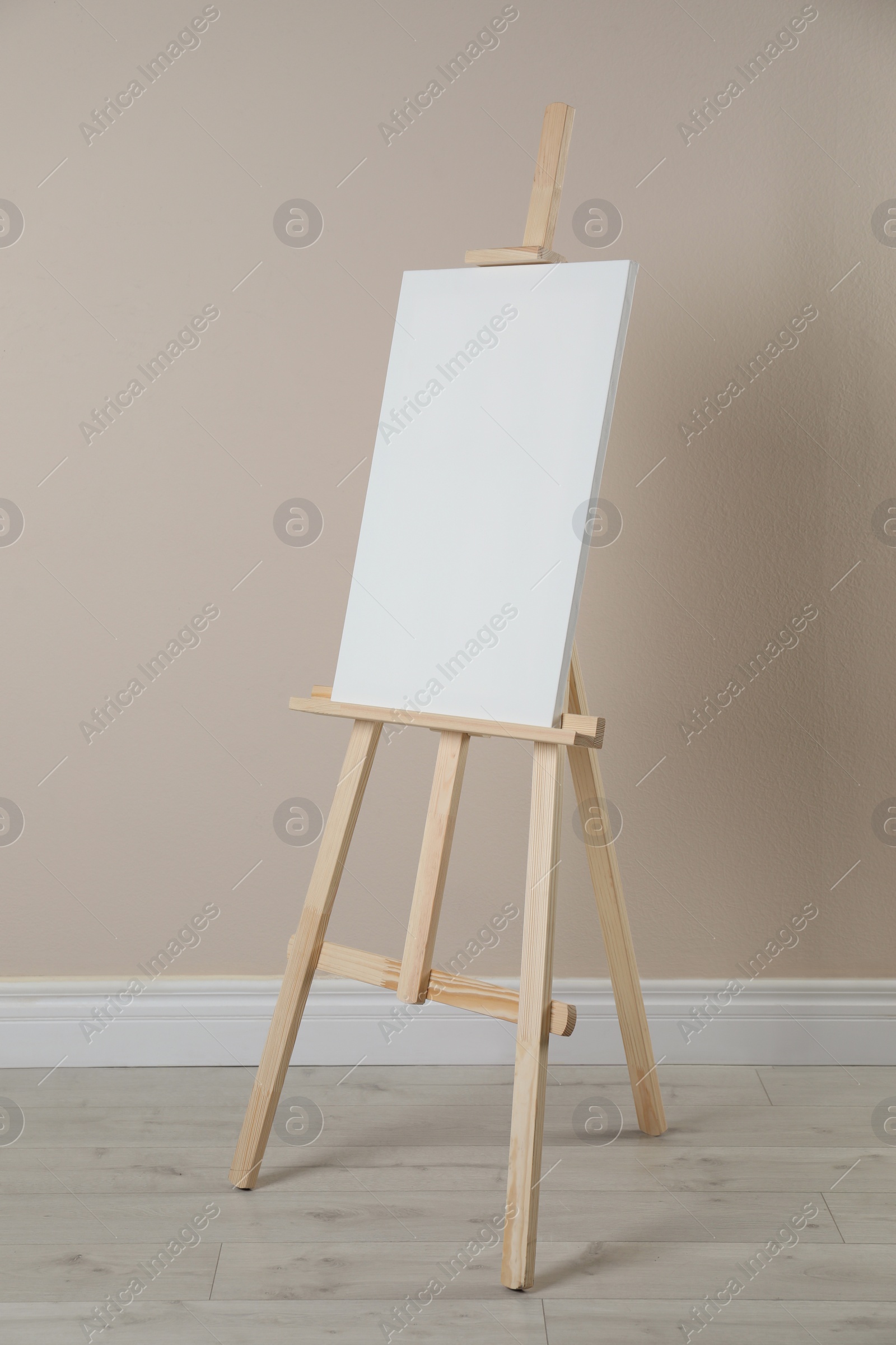 Photo of Wooden easel with blank canvas near beige wall