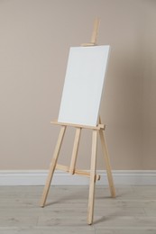 Photo of Wooden easel with blank canvas near beige wall