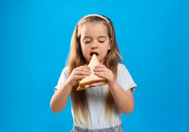 Cute little girl eating tasty sandwich on light blue background