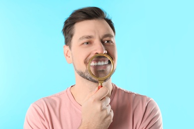 Smiling man with perfect teeth and magnifier on color background