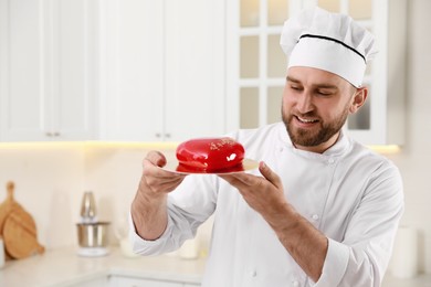 Photo of Happy professional confectioner holding delicious cake in kitchen