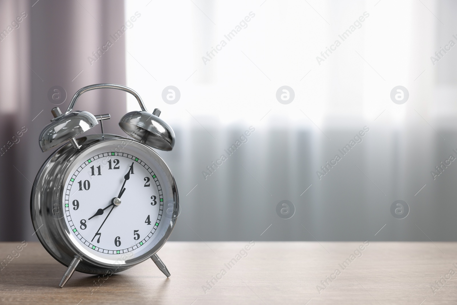 Photo of Silver alarm clock on wooden table indoors, space for text