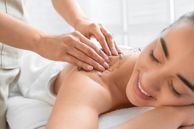 Photo of Young woman having body scrubbing procedure in spa salon, closeup