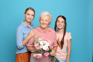 Photo of Happy sisters with their grandmother holding flowers on light blue background