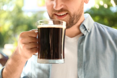 Photo of Young man with cold kvass outdoors, closeup. Traditional Russian summer drink