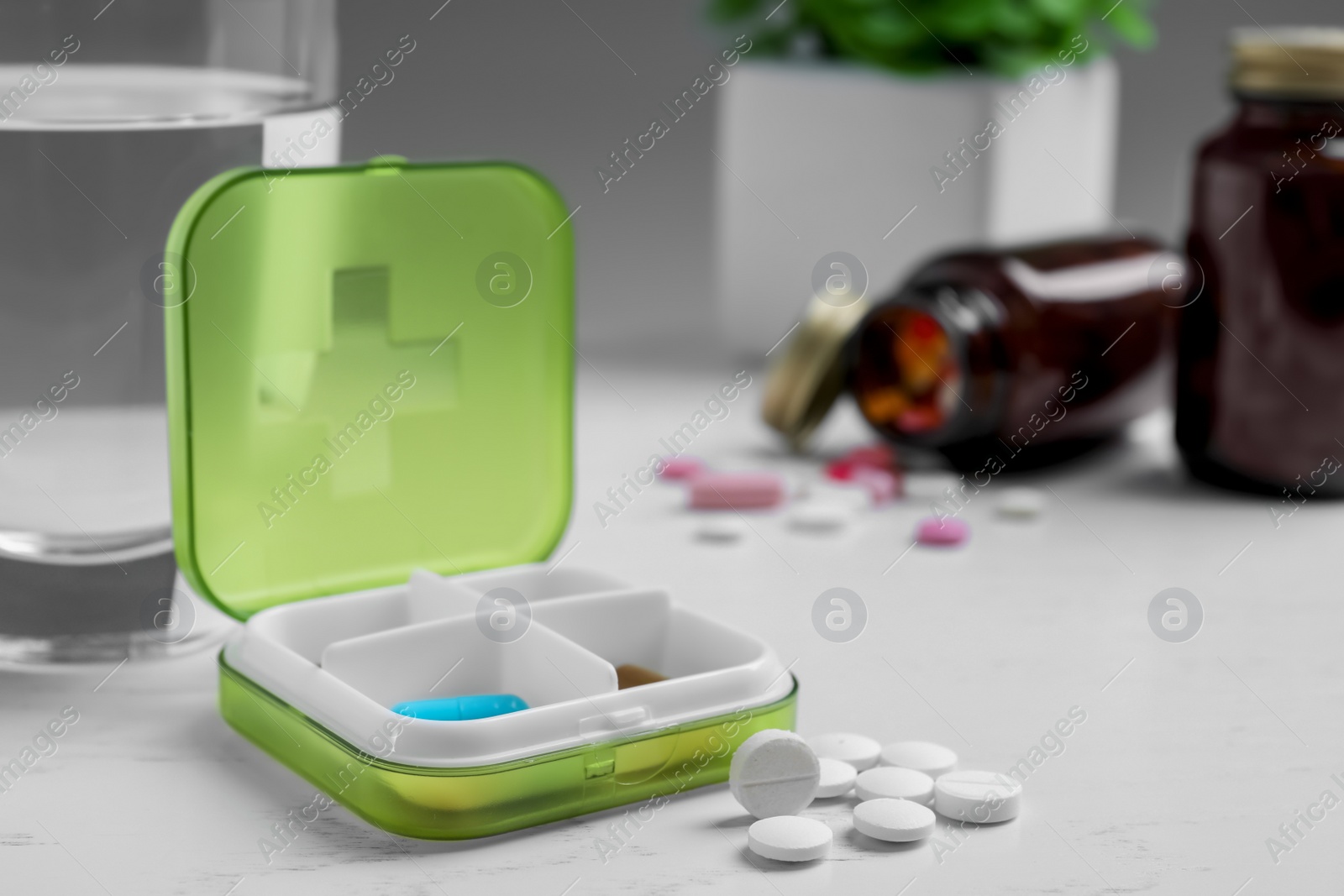 Photo of Pill box with medicaments and glass of water on white wooden table. Space for text