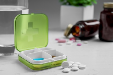 Pill box with medicaments and glass of water on white wooden table. Space for text