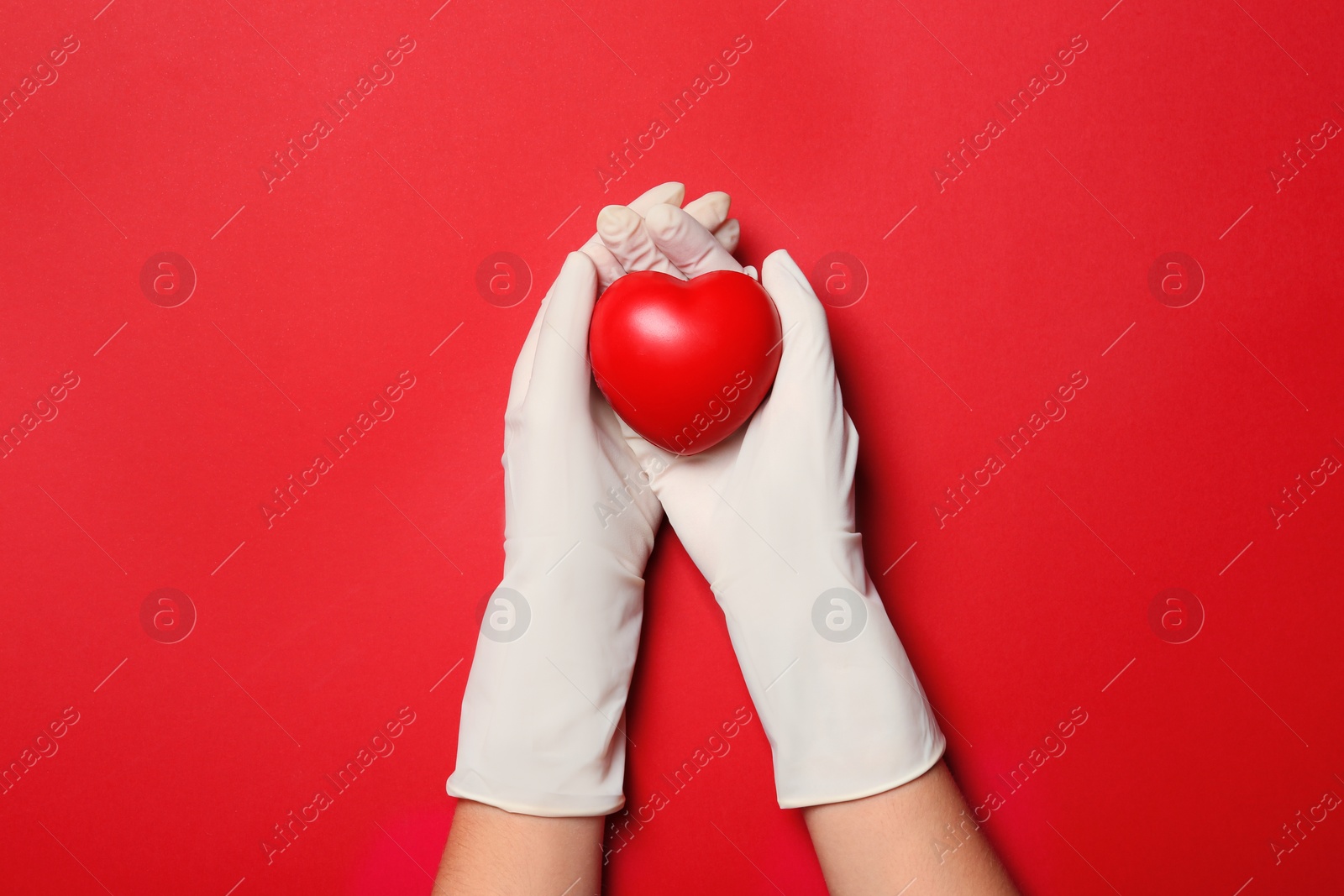 Photo of Doctor in medical gloves holding heart on color background, top view