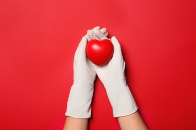 Photo of Doctor in medical gloves holding heart on color background, top view