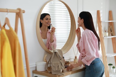 Young woman doing makeup near mirror at home. Morning routine
