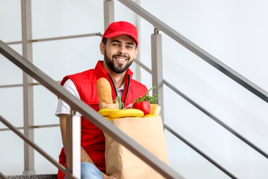 Photo of Man holding paper bag with fresh products on staircase. Food delivery service