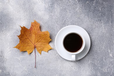 Cup of hot drink and autumn leaf on light grey textured table, flat lay