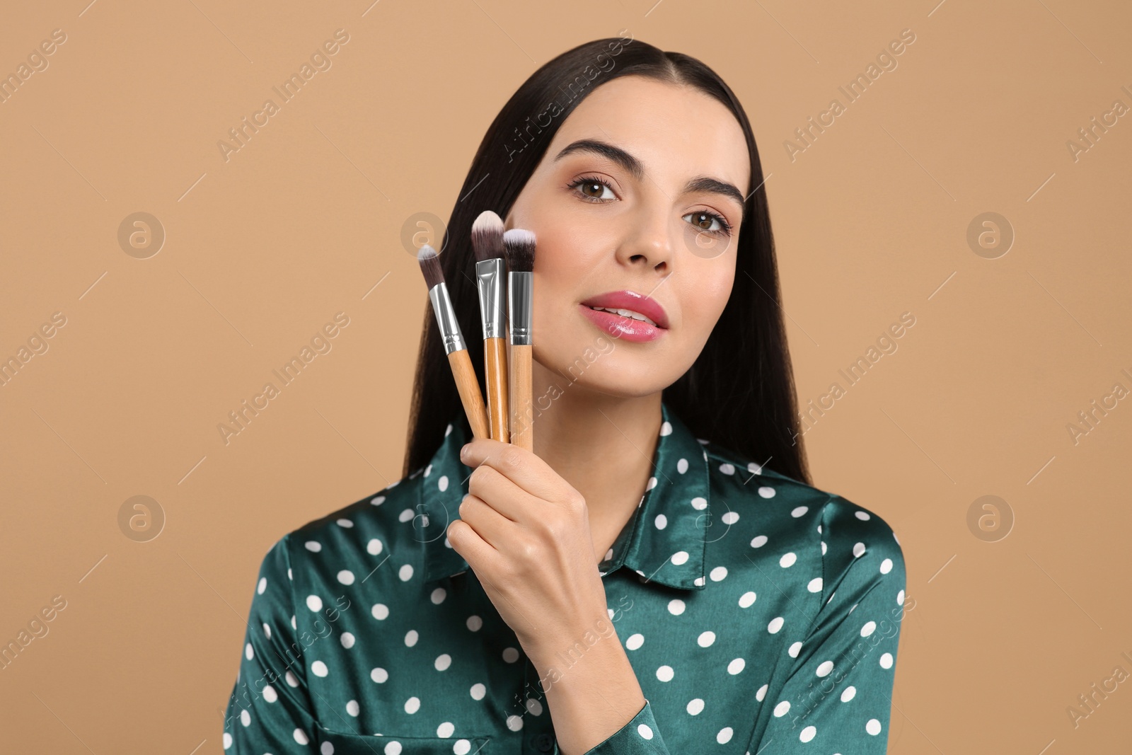 Photo of Beautiful woman with different makeup brushes on light brown background