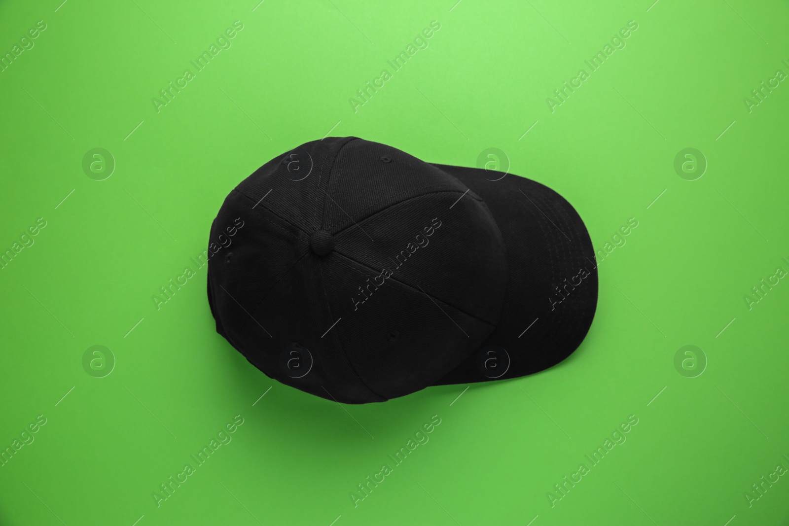 Photo of Stylish black baseball cap on light green background, top view