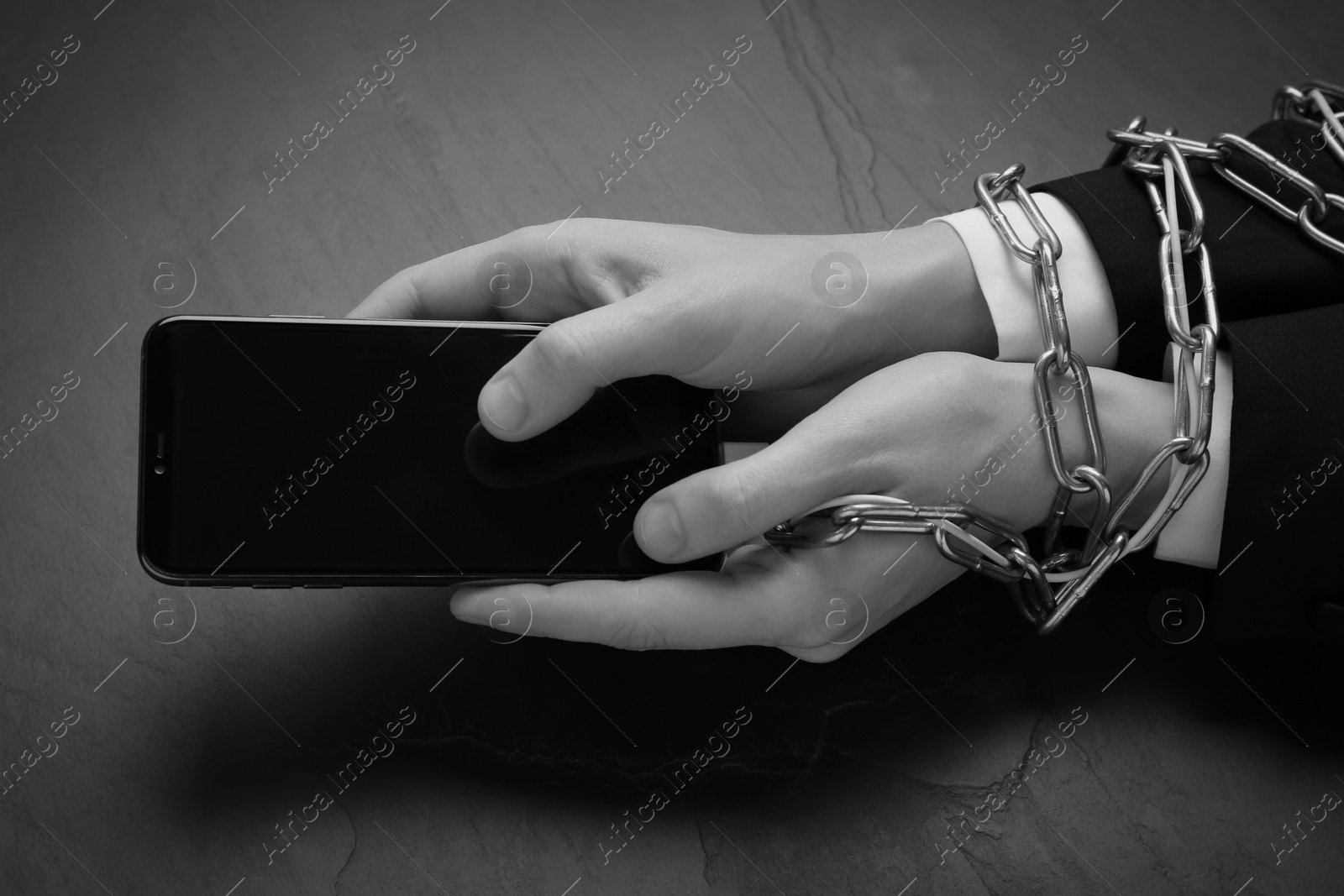 Image of Closeup view of internet addicted woman with chained hands using smartphone at dark table, space for text. Black and white effect
