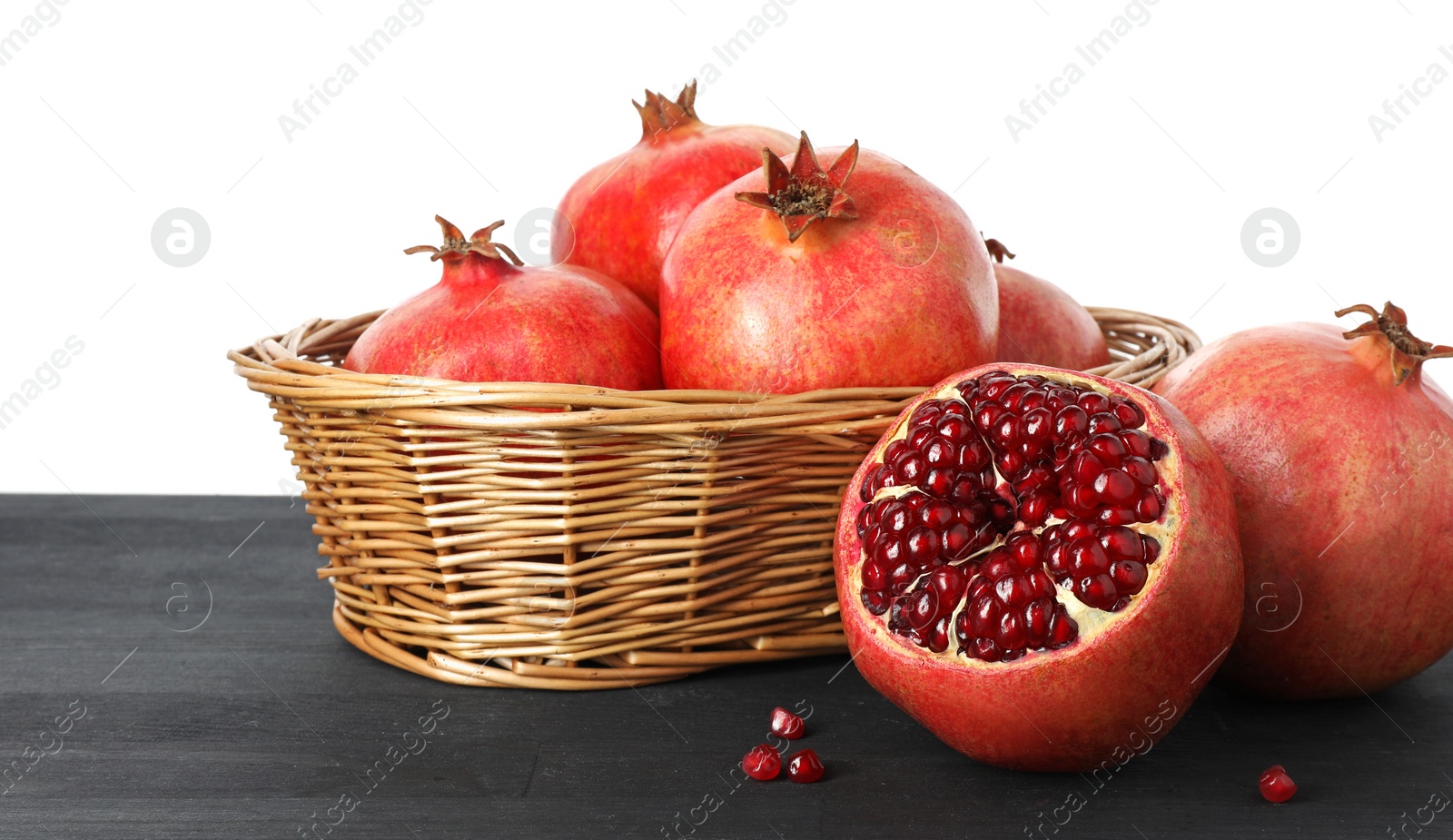 Photo of Fresh pomegranates in wicker basket on black wooden table against white background