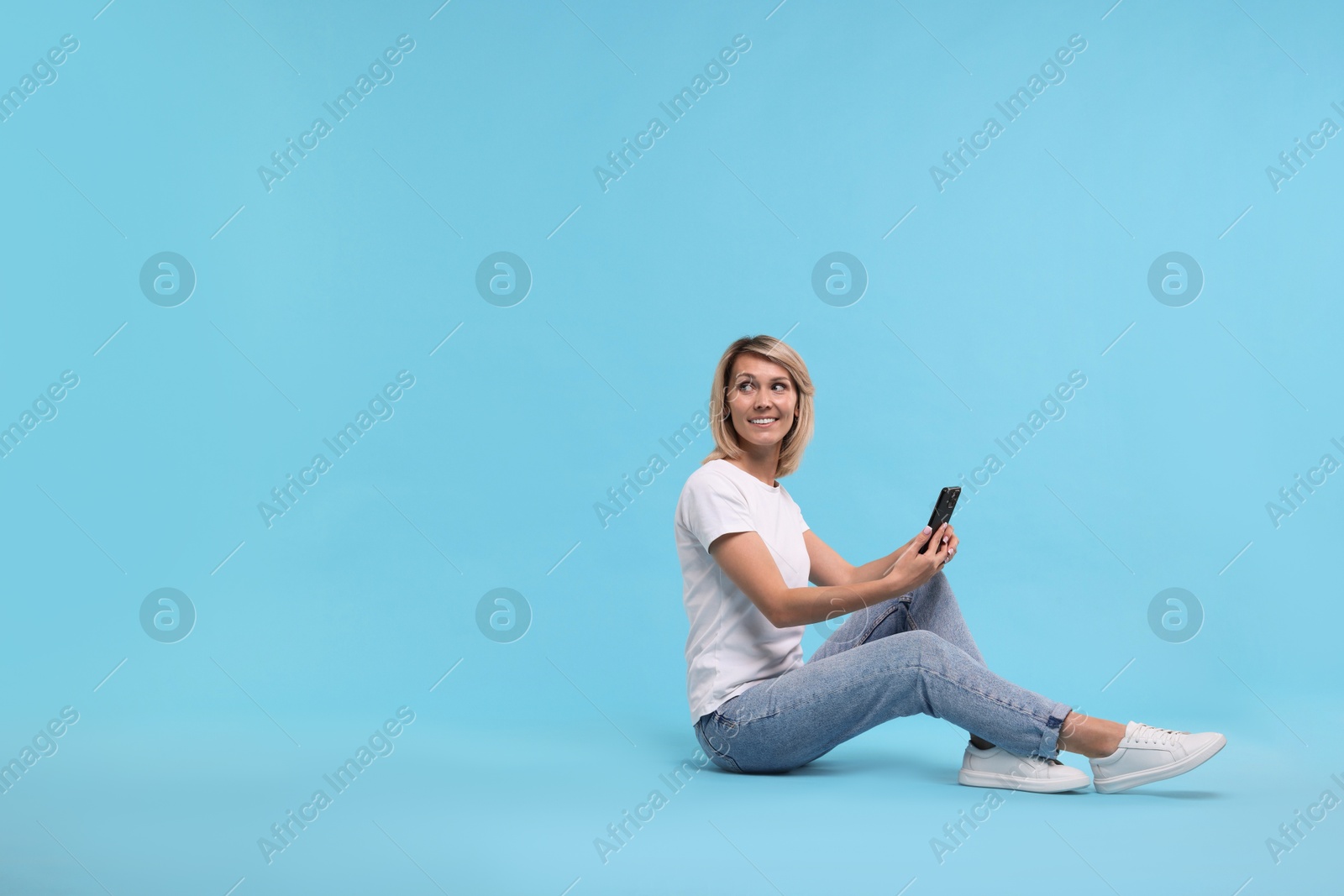 Photo of Happy woman with phone on light blue background, space for text