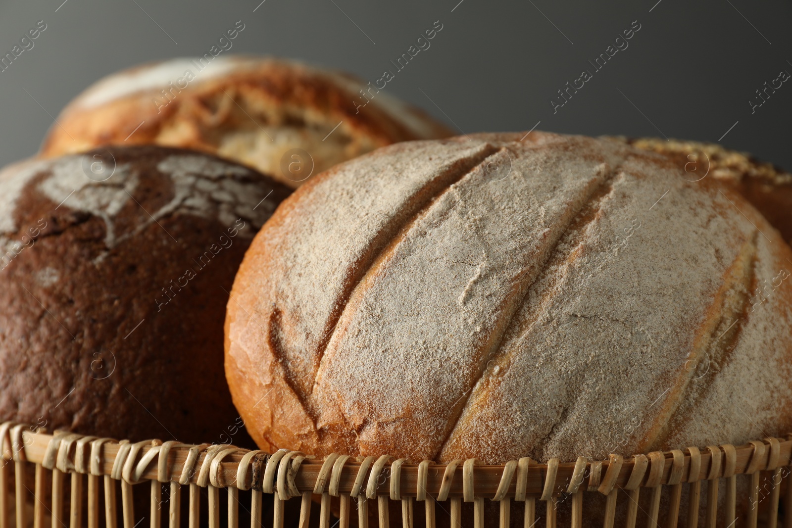 Photo of Wicker basket with different types of fresh bread against grey background, closeup
